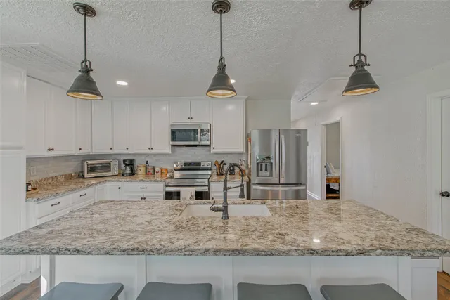 a kitchen with stainless steel appliances granite countertop a sink a refrigerator a stove a oven a counter space and cabinets