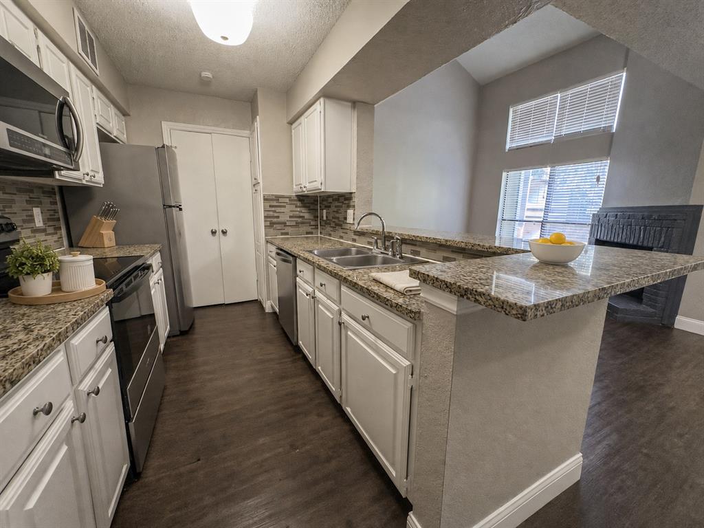 5840 Spring Valley Road, Unit 702 Dallas, TX 75254 - Photo 6 of 15 Kitchen featuring granite countertops, white cabinetry, stainless steel appliances, a tile backsplash, and wood-finish flooring
