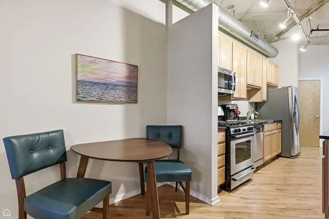 a kitchen with stainless steel appliances kitchen island a table chairs and a refrigerator