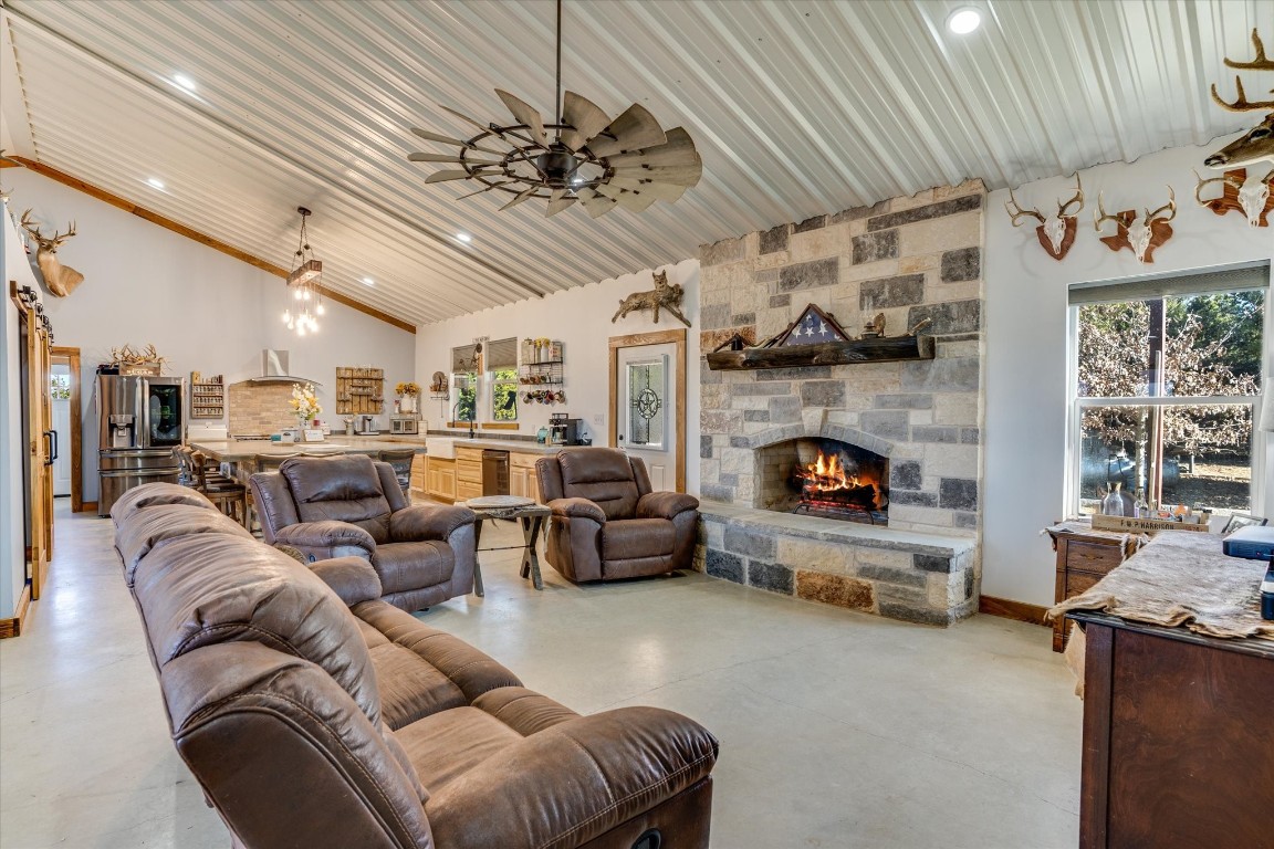 Living room featuring ceiling fan, a stone fireplace, and high vaulted ceiling