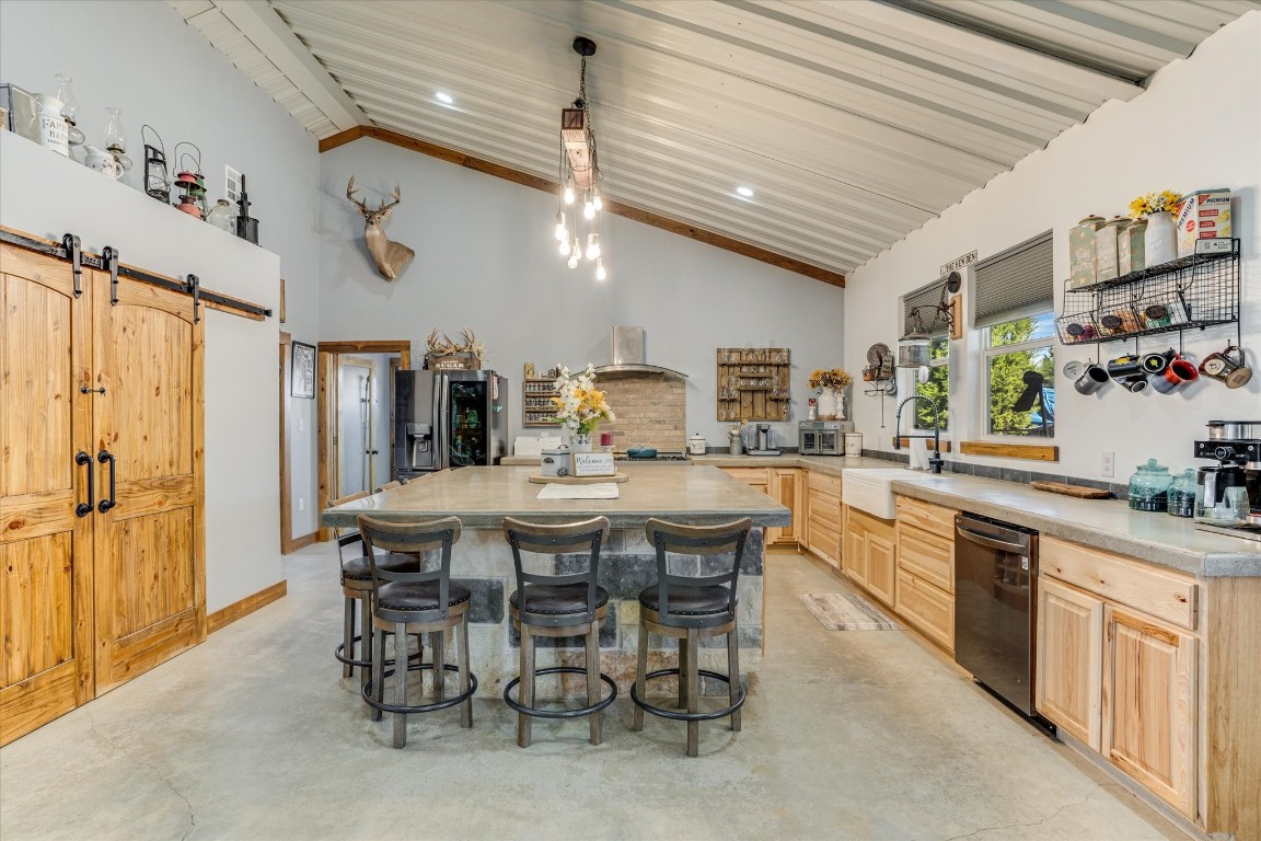 Kitchen featuring a barn door, stainless steel fridge, black dishwasher, light brown cabinets, and sink