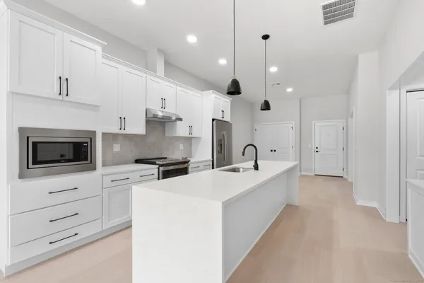 a large kitchen with stainless steel appliances a refrigerator a sink dishwasher a oven and a dining table with wooden floor