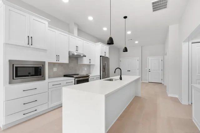 a large kitchen with stainless steel appliances a refrigerator a sink dishwasher a oven and a dining table with wooden floor