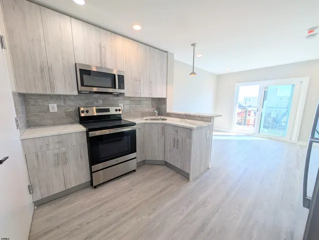 a kitchen with stainless steel appliances a white stove top oven a sink dishwasher and a refrigerator with wooden floor