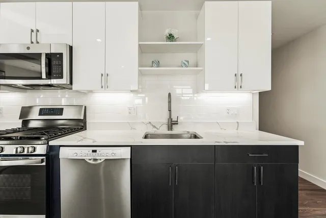 a kitchen with stainless steel appliances granite countertop a refrigerator a sink a stove top oven a dining table and chairs with wooden floor