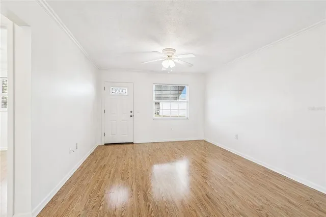 an empty room with wooden floor chandelier fan and windows