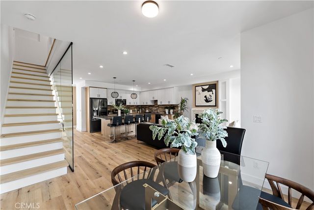 a open kitchen with stainless steel appliances kitchen island granite countertop a refrigerator a sink a stove and a dining table with wooden floor