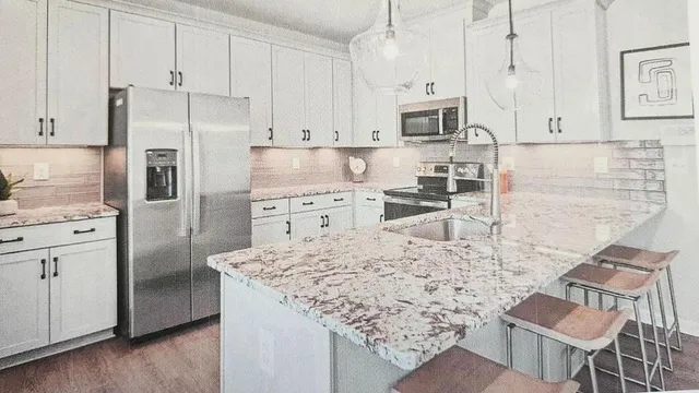 a kitchen with stainless steel appliances kitchen island granite countertop a refrigerator a stove a sink and white cabinets