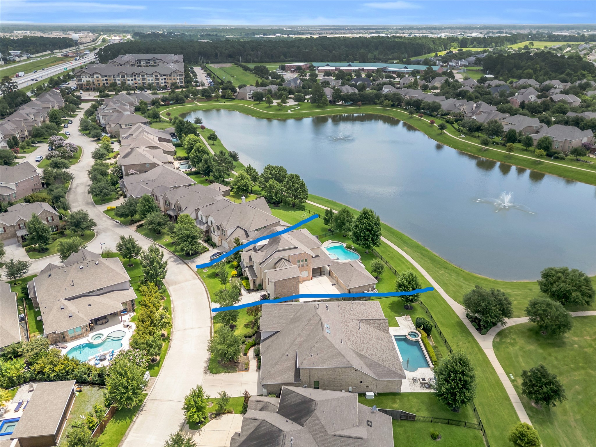 9842 Kirkstone Terrace Drive Spring, TX 77379 - Photo 29 of 34 a beautiful lakeside property in a serene neighborhood. The home features a spacious backyard with a pool and is situated along a picturesque lake with a fountain. The surrounding area is lush with greenery, offering a peaceful and scenic environment. Nearby, there is convenient access to roads and community amenities.