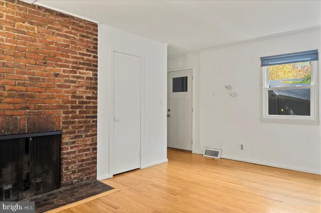 a view of an empty room with wooden floor and a fireplace