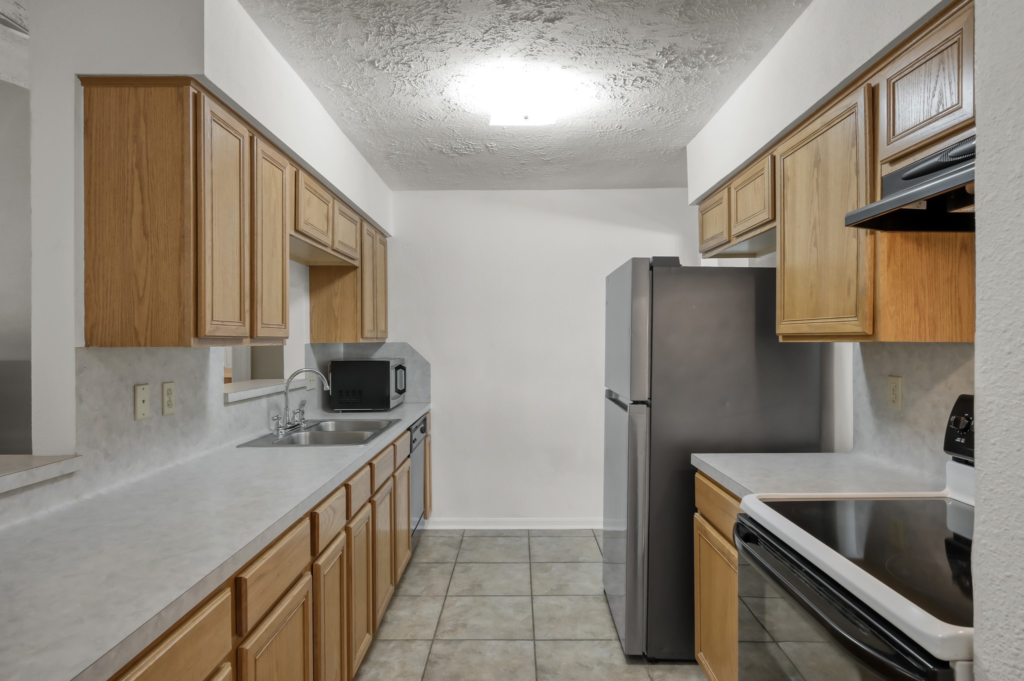 4314 Enchantedgate Drive Spring, TX 77373 - Photo 11 of 47 Kitchen features a galley layout with light wood cabinets, a stainless steel refrigerator, and modern appliances. With ample countertop space and a neutral tile floor, creating a clean and functional cooking area.