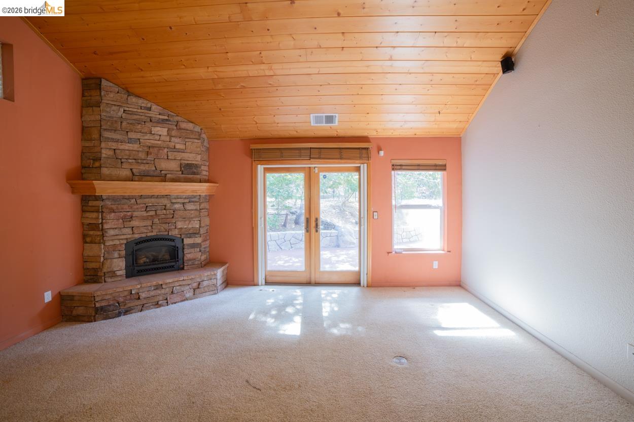 Corner stone fireplace with wood mantel, wood plank ceiling, and exterior access via double glass doors