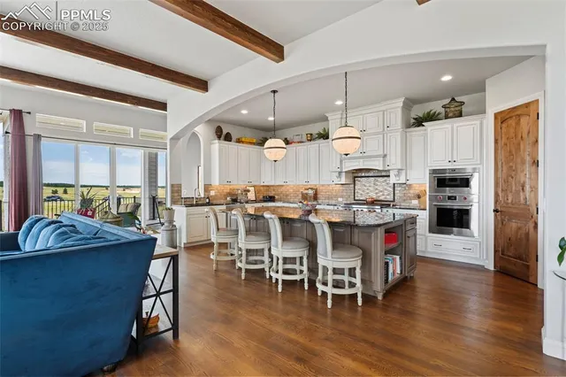 a dining hall with stainless steel appliances kitchen island granite countertop a table chairs and a living room
