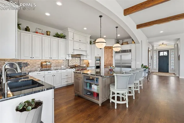 a kitchen with stainless steel appliances kitchen island granite countertop a stove a sink a refrigerator and white cabinets with wooden floor