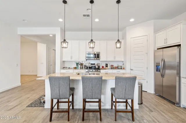 a kitchen with kitchen island a dining table chairs wooden floor cabinets and appliances