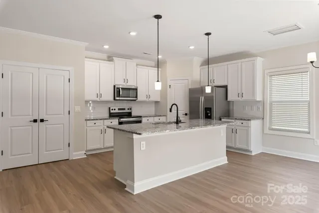 a kitchen with stainless steel appliances granite countertop a sink a stove a refrigerator and white cabinets with wooden floor