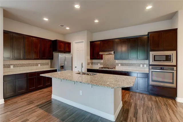 a large kitchen with stainless steel appliances wooden cabinets and a stove top oven
