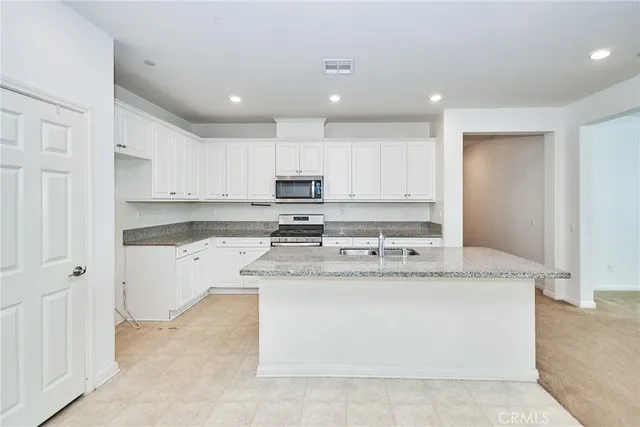 a large kitchen with stainless steel appliances granite countertop a stove a sink a refrigerator and white cabinets with wooden floor