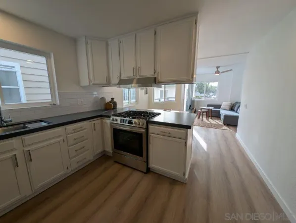 a kitchen with a sink dishwasher a stove and white cabinets with wooden floor