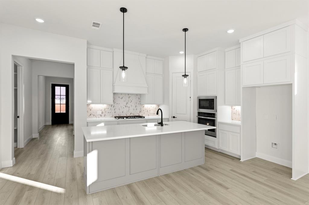 1105 Birdsong Trail Anna, TX 75409 - Photo 8 of 27 a large kitchen with kitchen island a stove a sink a refrigerator and white cabinets with wooden floor