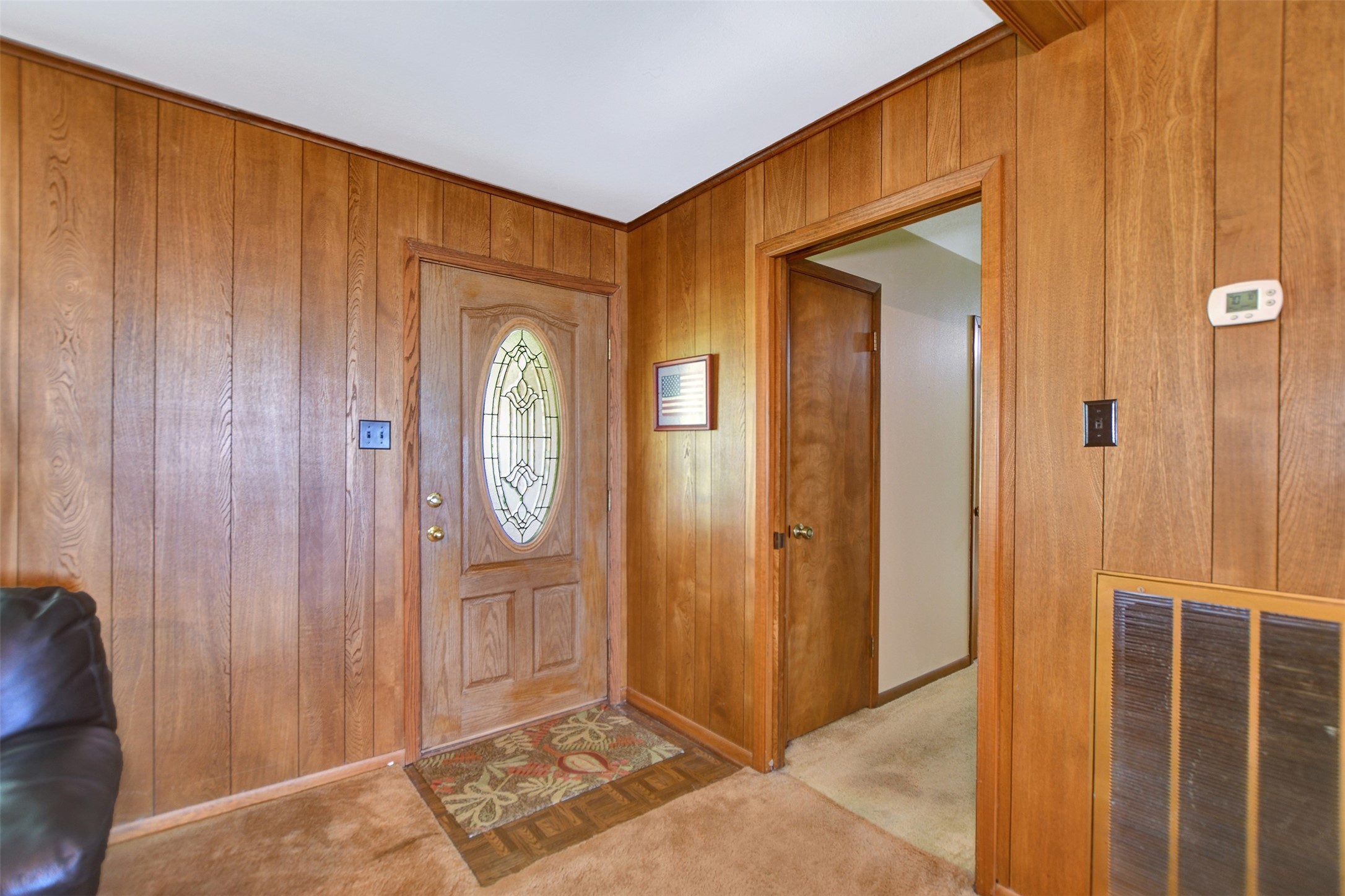 341 South S Loop Bellville, TX 77418 - Photo 5 of 33 This cozy entryway features warm wood paneling and a decorative oval glass front door, leading to a hallway with carpeted flooring and simple, classic details.