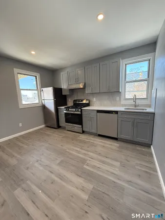 a kitchen with stainless steel appliances granite countertop a sink a stove a refrigerator with grey cabinets and wooden floor
