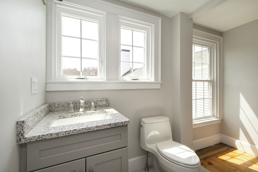 128 Washington Street, Unit F Hanover, MA 02339 - Photo 35 of 42 a bathroom with a granite countertop sink toilet and mirror next to a window
