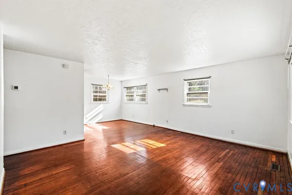 an empty room with wooden floor chandelier and windows