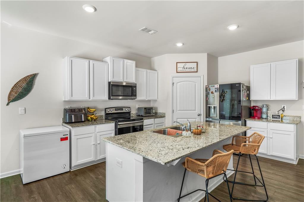 499 Walnut Grv Way Pendergrass, GA 30567 - Photo 7 of 19 a kitchen with stainless steel appliances kitchen island granite countertop a refrigerator a stove top oven a sink dishwasher and white cabinets with wooden floor