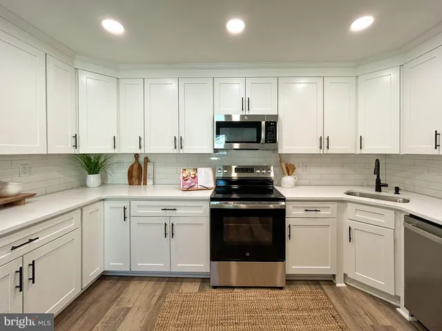 a kitchen with cabinets stainless steel appliances a sink and wooden floor