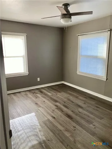 an empty room with wooden floor ceiling fan and windows