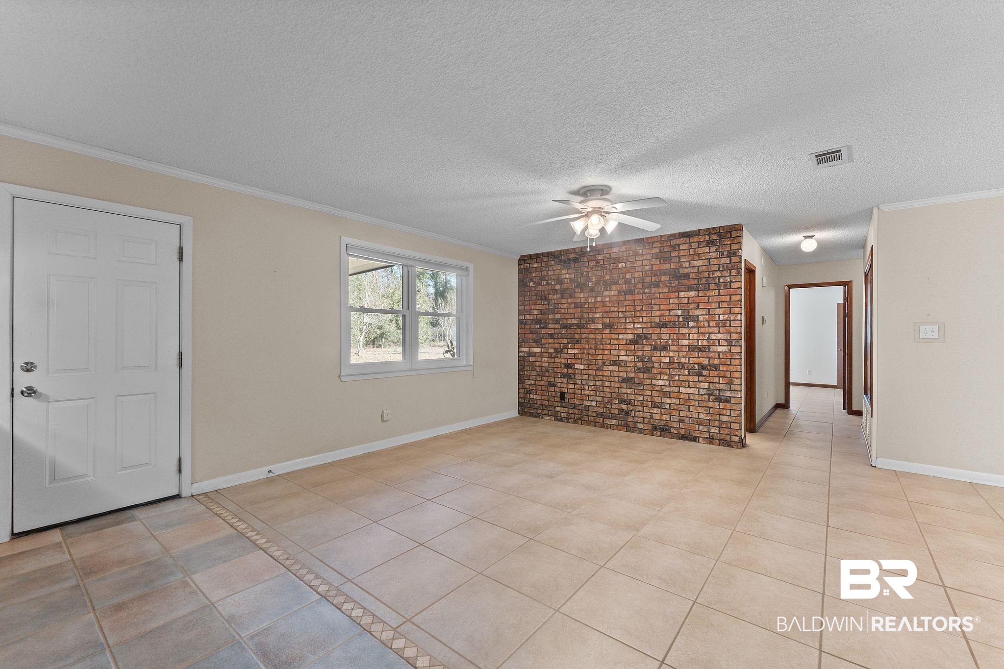 32989 Antietam Road Lillian, AL 36549 - Photo 5 of 56 Unfurnished living room featuring brick wall, crown molding, a ceiling fan, a textured ceiling, and light tile patterned floors