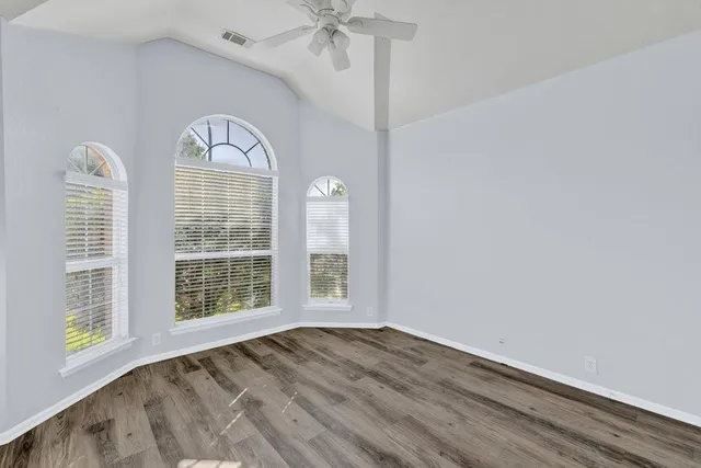 an empty room with wooden floor fan and windows