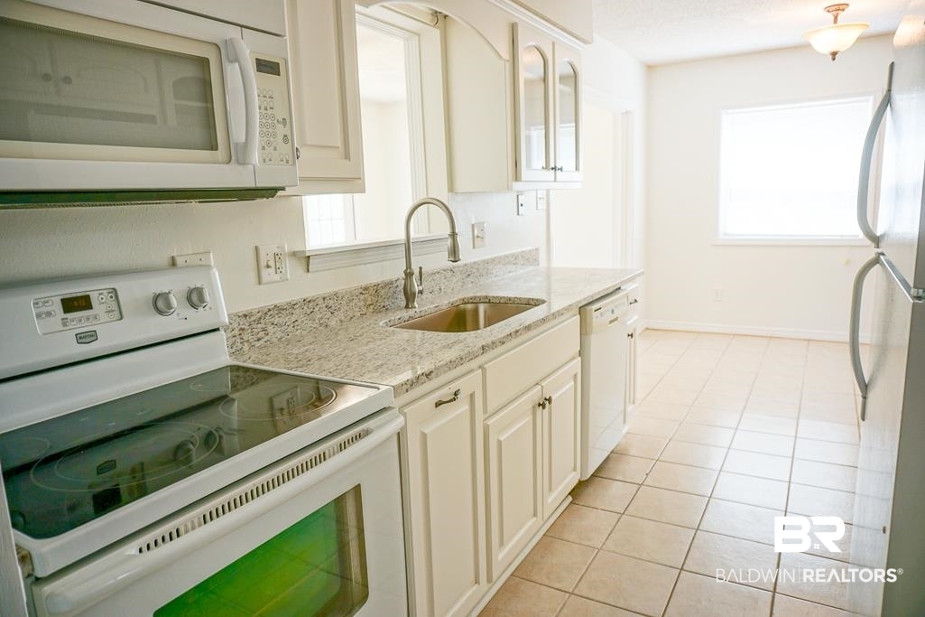 4377 Fathbrook Lane Mobile, AL 36693 - Photo 8 of 19 Kitchen with white appliances, light tile patterned floors, a sink, light stone countertops, and glass insert cabinets