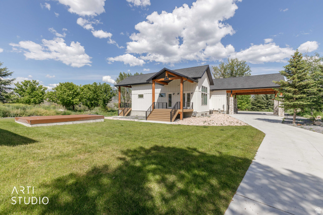 1188 South Old Trappers Loop Road Huntsville, UT 84317 - Photo 3 of 92 Modern farmhouse exterior featuring white vertical siding, a dark pitched roof, wood-finish columns, a covered front porch with wood-finish steps, and a concrete driveway leading to a covered carport with stone pillar supports