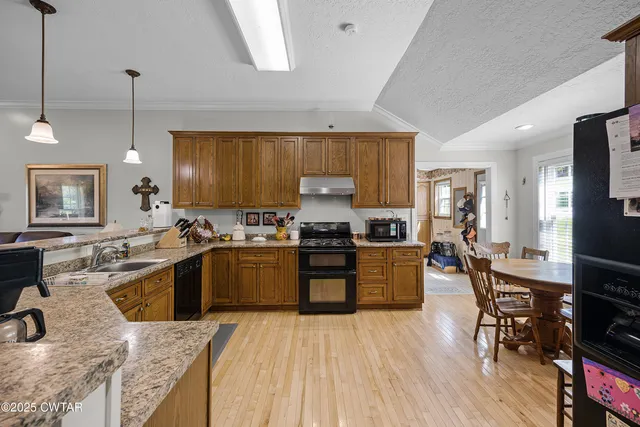 a kitchen with stainless steel appliances granite countertop wooden cabinets a sink a stove a dining table and chairs