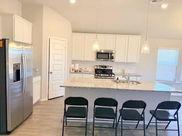 a kitchen with stainless steel appliances granite countertop a table chairs refrigerator and sink