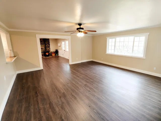 an empty room with wooden floor ceiling fan and windows