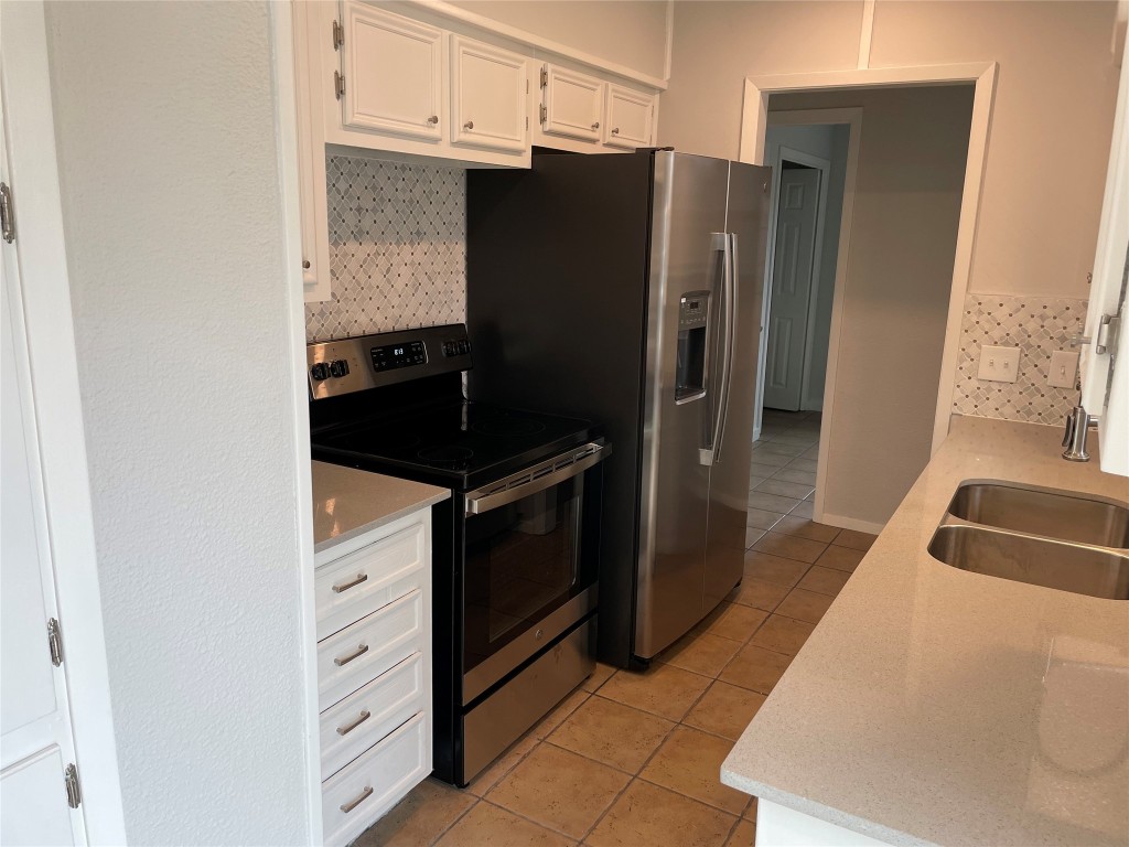 4619 Jinx Avenue, Unit A Austin, TX 78745 - Photo 6 of 15 Kitchen featuring decorative backsplash, appliances with stainless steel finishes, white cabinets, light tile patterned floors, and light stone counters