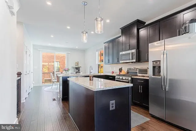 a kitchen with granite countertop a refrigerator a sink a stove and oven with wooden floor