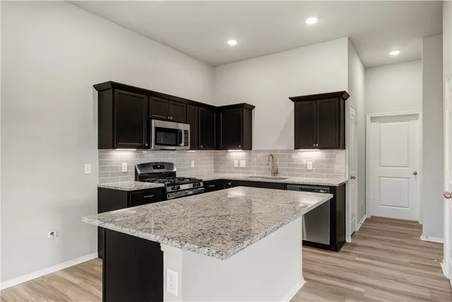 a kitchen with stainless steel appliances granite countertop a sink dishwasher a stove and a microwave oven with wooden floor