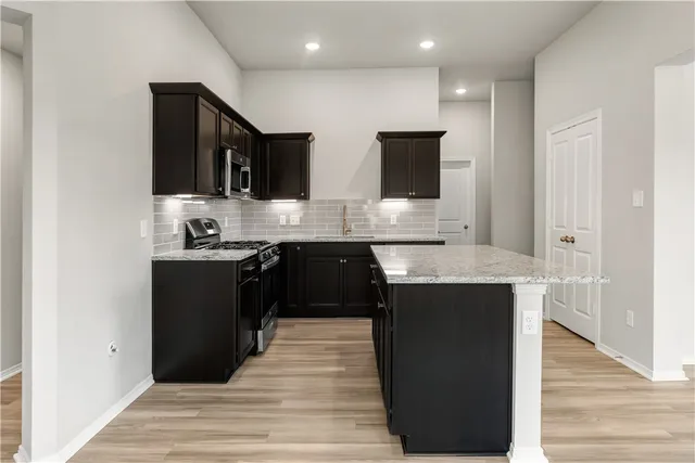 a kitchen with stainless steel appliances granite countertop a refrigerator a sink and a stove with wooden floor