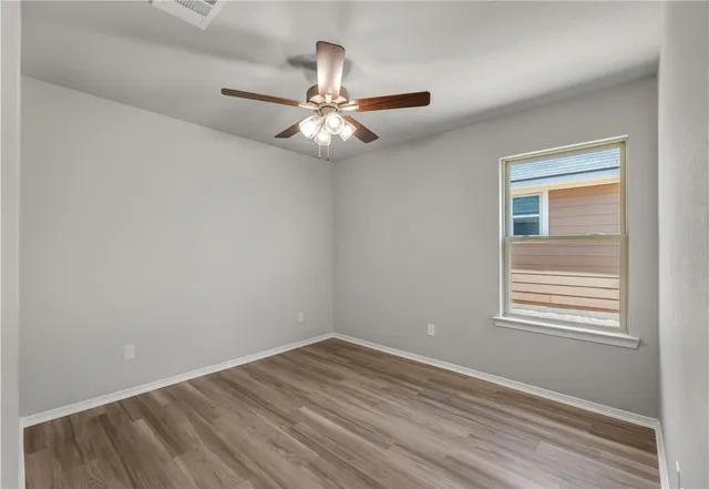 an empty room with wooden floor fan and windows