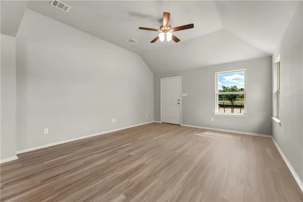 an empty room with wooden floor ceiling fan and windows