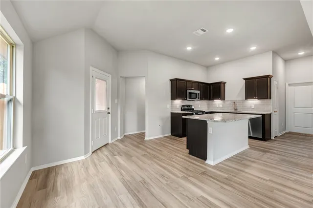 a kitchen with stainless steel appliances granite countertop a stove top oven a sink dishwasher a refrigerator and white cabinets with wooden floor