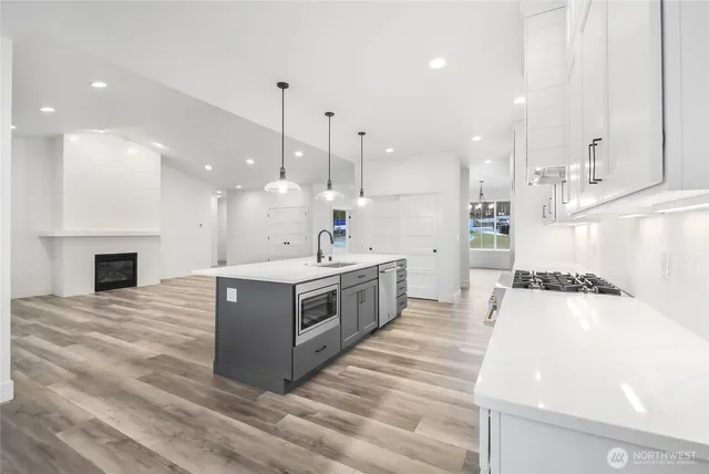 a large white kitchen with a stove a sink dishwasher and a fireplace with wooden floor