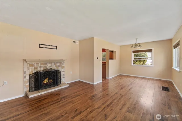 a view of an empty room with wooden floor fireplace and a window