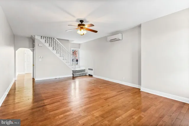a view of an empty room with wooden floor and a ceiling fan