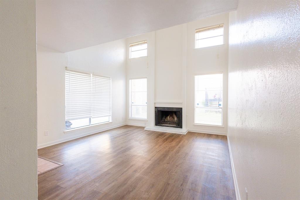 5540 Boca Raton Boulevard, Unit 175 Fort Worth, TX 76112 - Photo 3 of 30 Unfurnished living room featuring a textured wall, a fireplace with raised hearth, wood finished floors, and a high ceiling