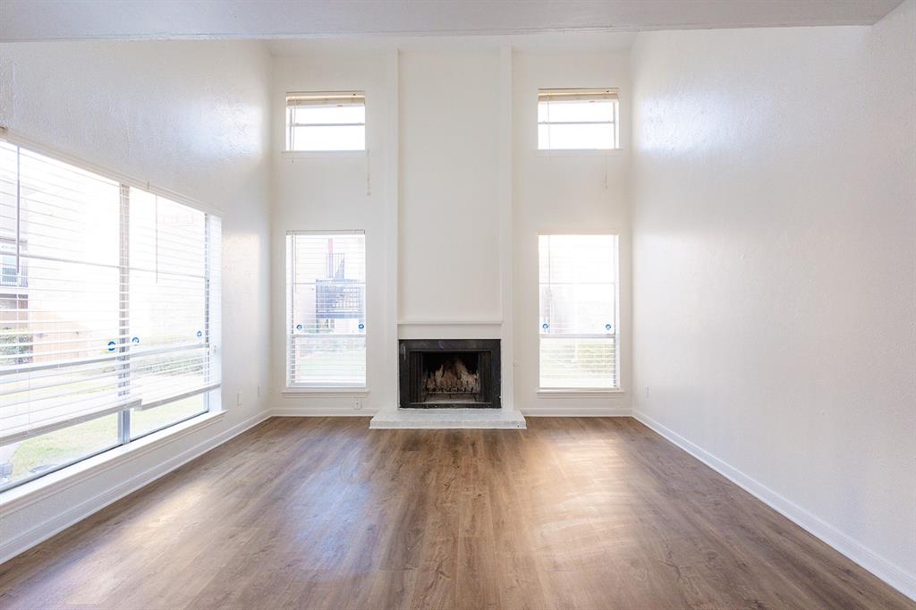 5540 Boca Raton Boulevard, Unit 175 Fort Worth, TX 76112 - Photo 4 of 30 Unfurnished living room featuring a fireplace with raised hearth, wood finished floors, and a high ceiling
